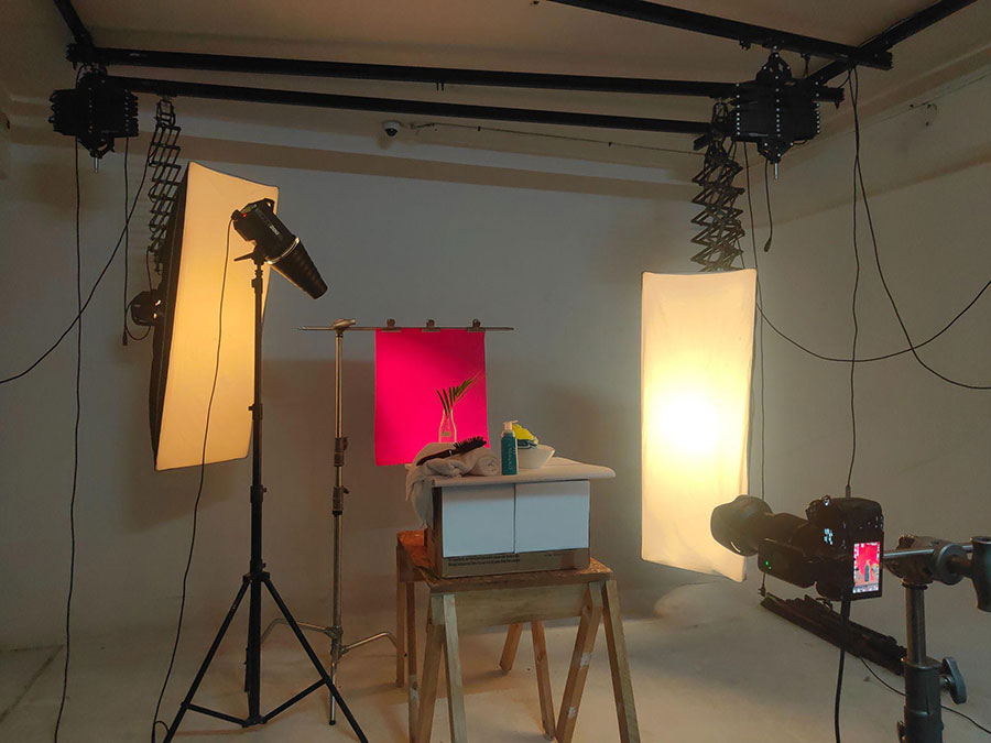 A behind-the-scenes photograph of a studio setup for product photography, featuring a tabletop display with a bottle and a hairbrush set against a vibrant pink background