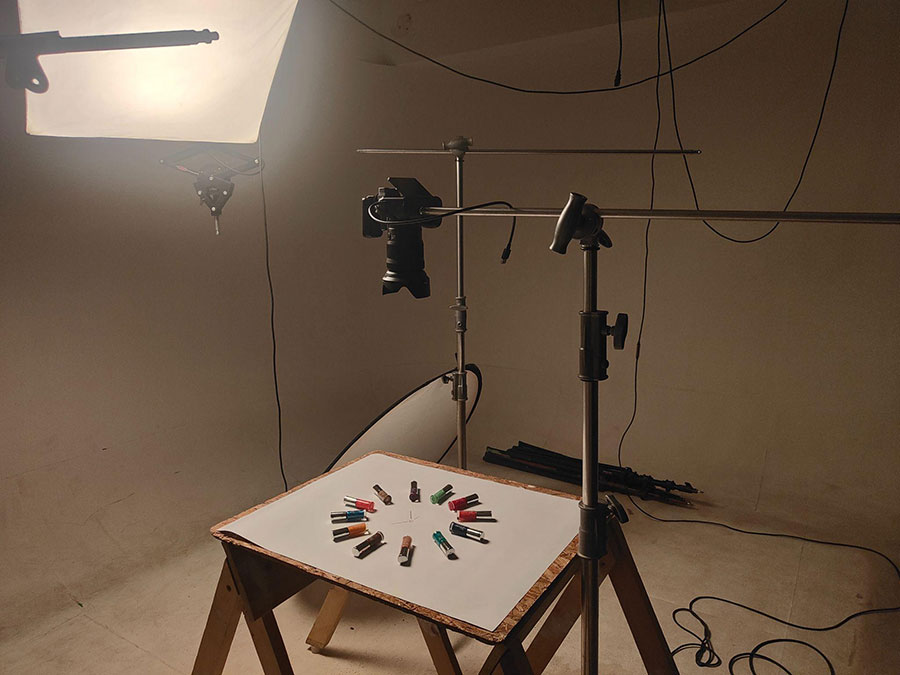 A behind-the-scenes photograph of a studio setup for product photography, showcasing a top-down view of small product containers arranged in a circle on a white tabletop